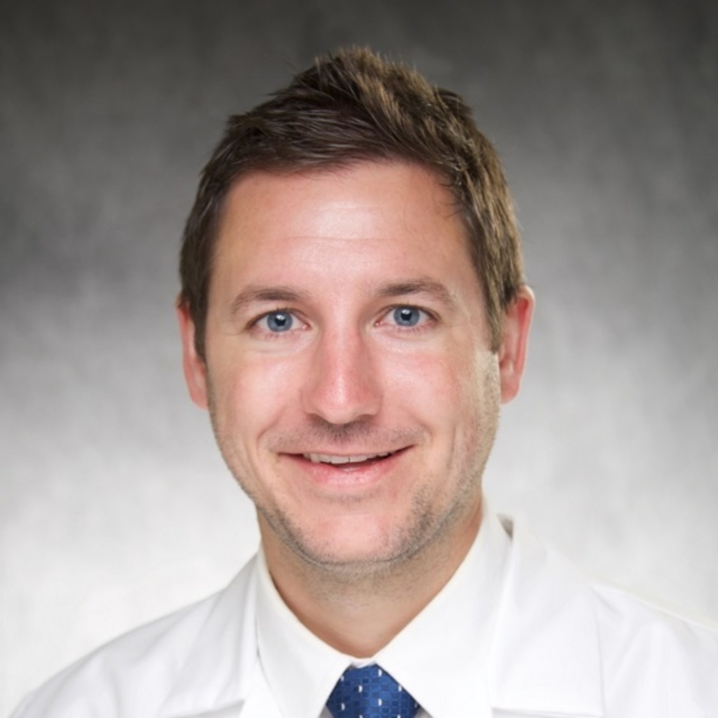 A photo of Dr. Nick Trapp wearing a white coat, white shirt, and tie in front of a gray background