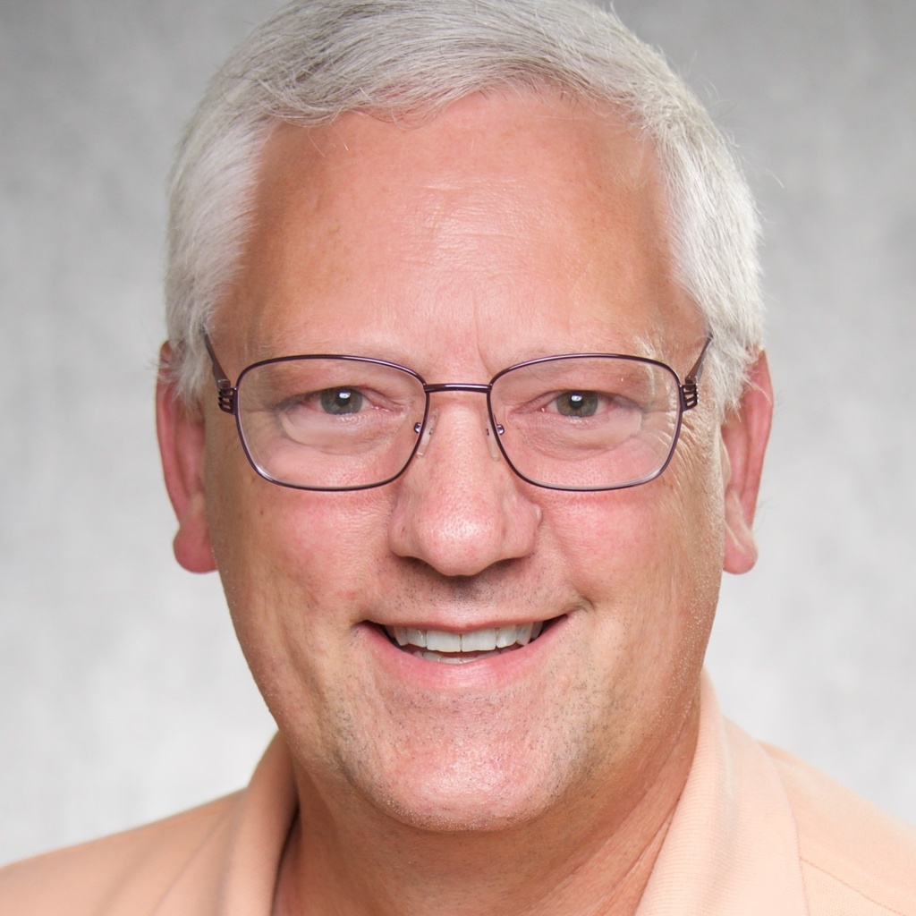 A photo of Ken Manzel smiling and wearing a peach shirt