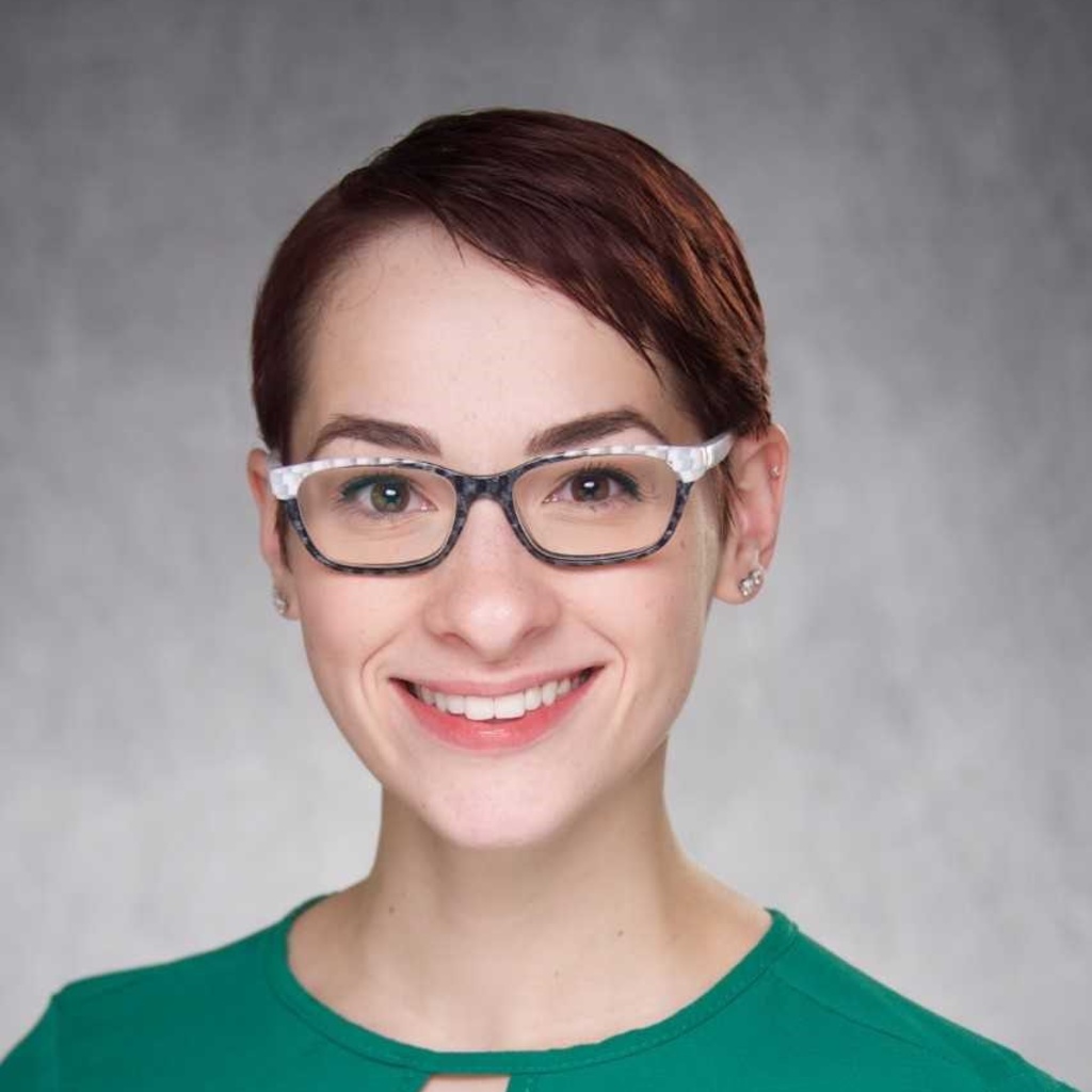 A photo of Kathleen Langbehn smiling, wearing a green shirt in front of a gray background