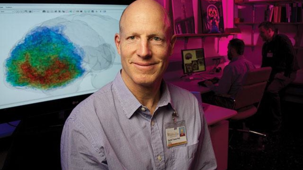 A photo of Dr. Daniel Tranel sitting in front of a computer displaying a brain scan